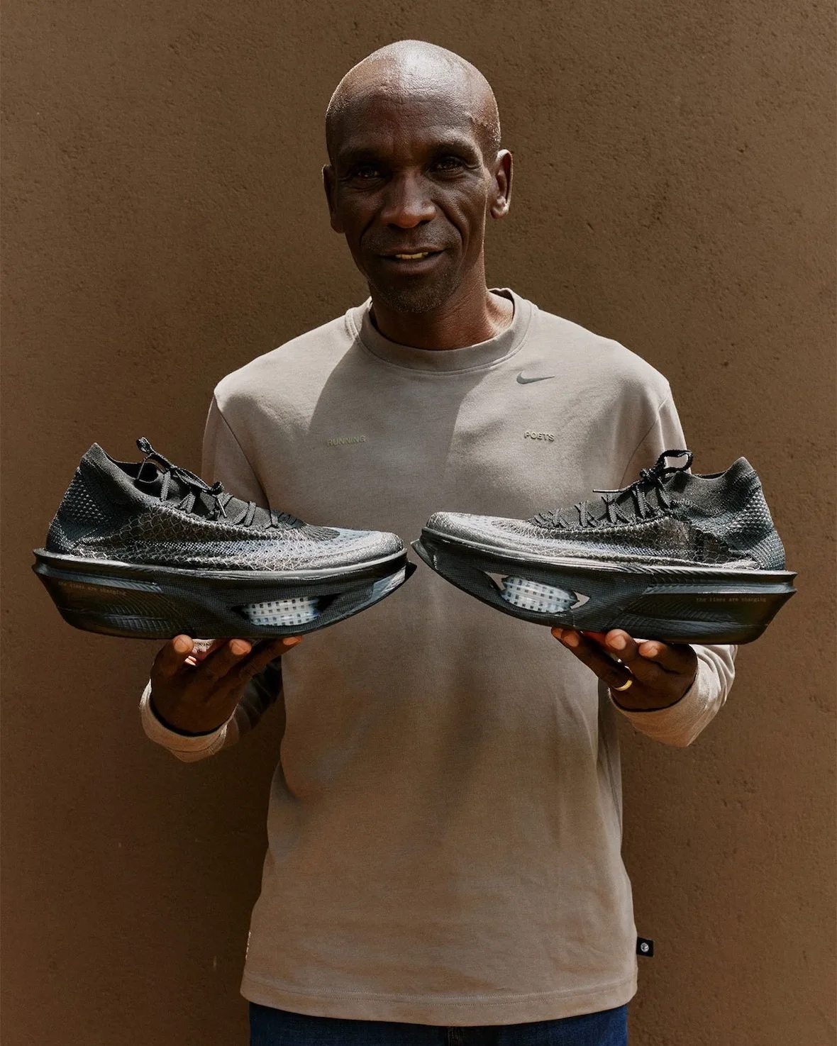 man in a nike sweatshirt holding a pair of the shoes, beige studio backdrop, Nike Apex