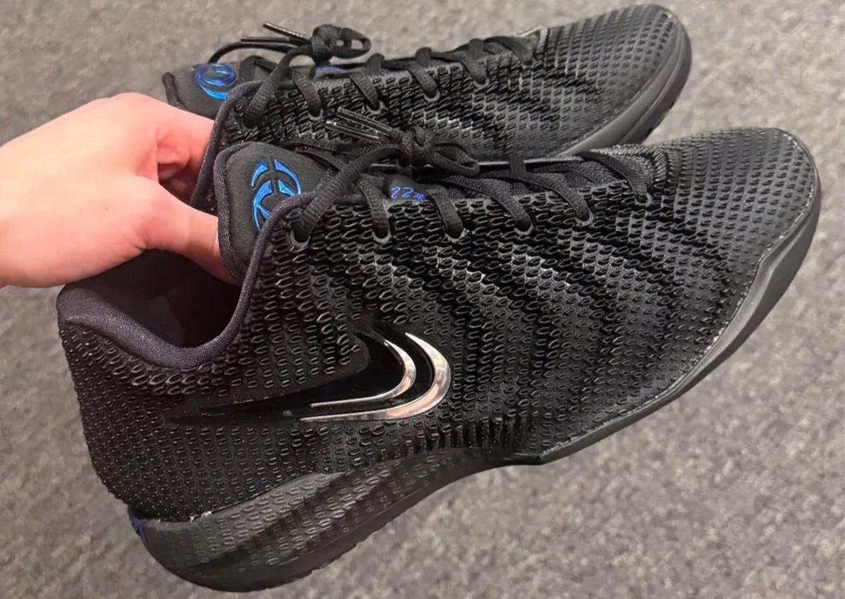 in-hand pair, lateral view, black textured upper with chrome swoosh and blue tongue logo, Nike Caitlin 1 “3x Black”