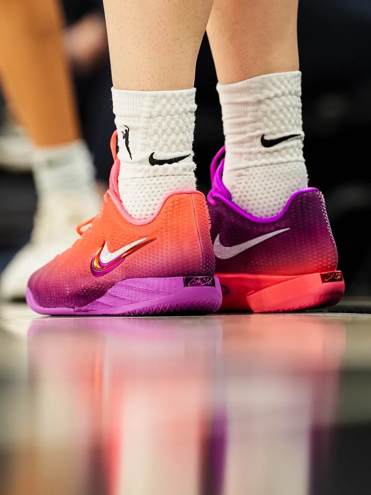 On-foot heel view, purple shoe on left, pink-orange shoe on right, reflective floor, Berry Fade