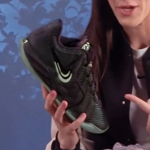 in-hand medial view held by a person, black textured upper with mint green swoosh and outsole, Halloween