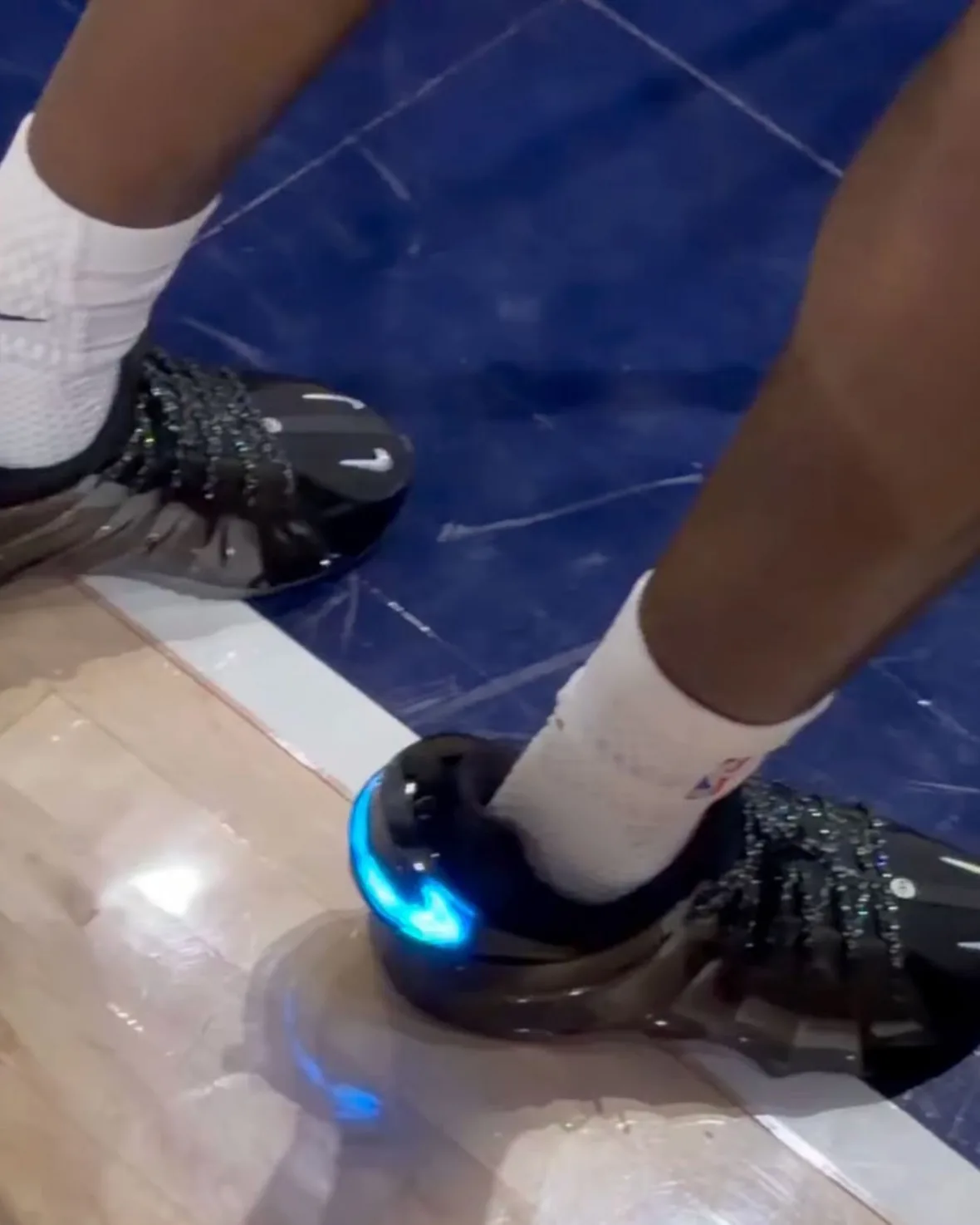 on-foot pair from above on court, black shoes with glowing blue swoosh, Nike GT Flight