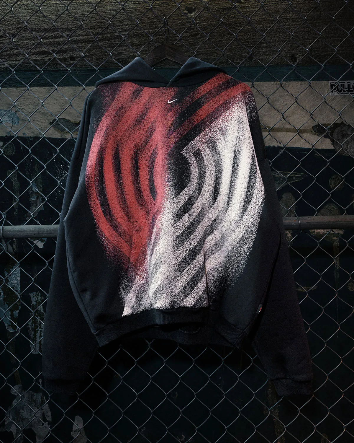 hanging on chain-link fence, black hoodie with red and white spray-paint graphic, Standard Issue Collection
