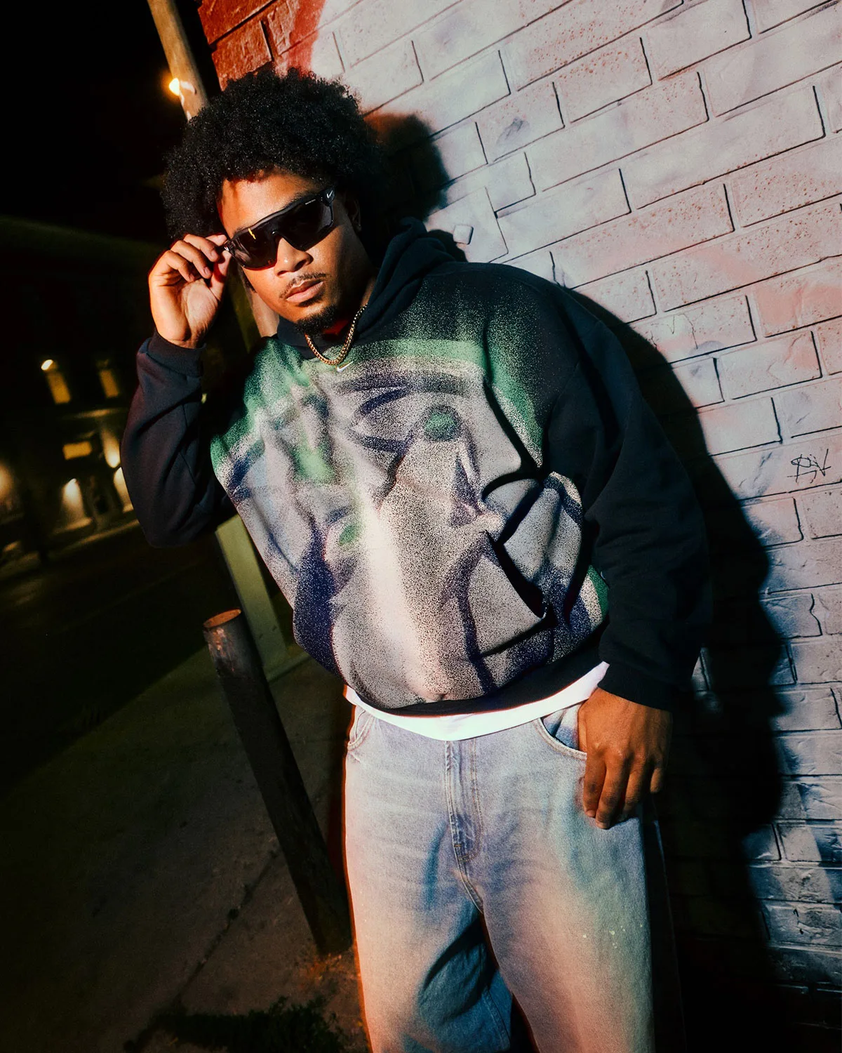 on-body, black hoodie with green and grey spray-paint graphic, brick wall backdrop, Standard Issue Collection