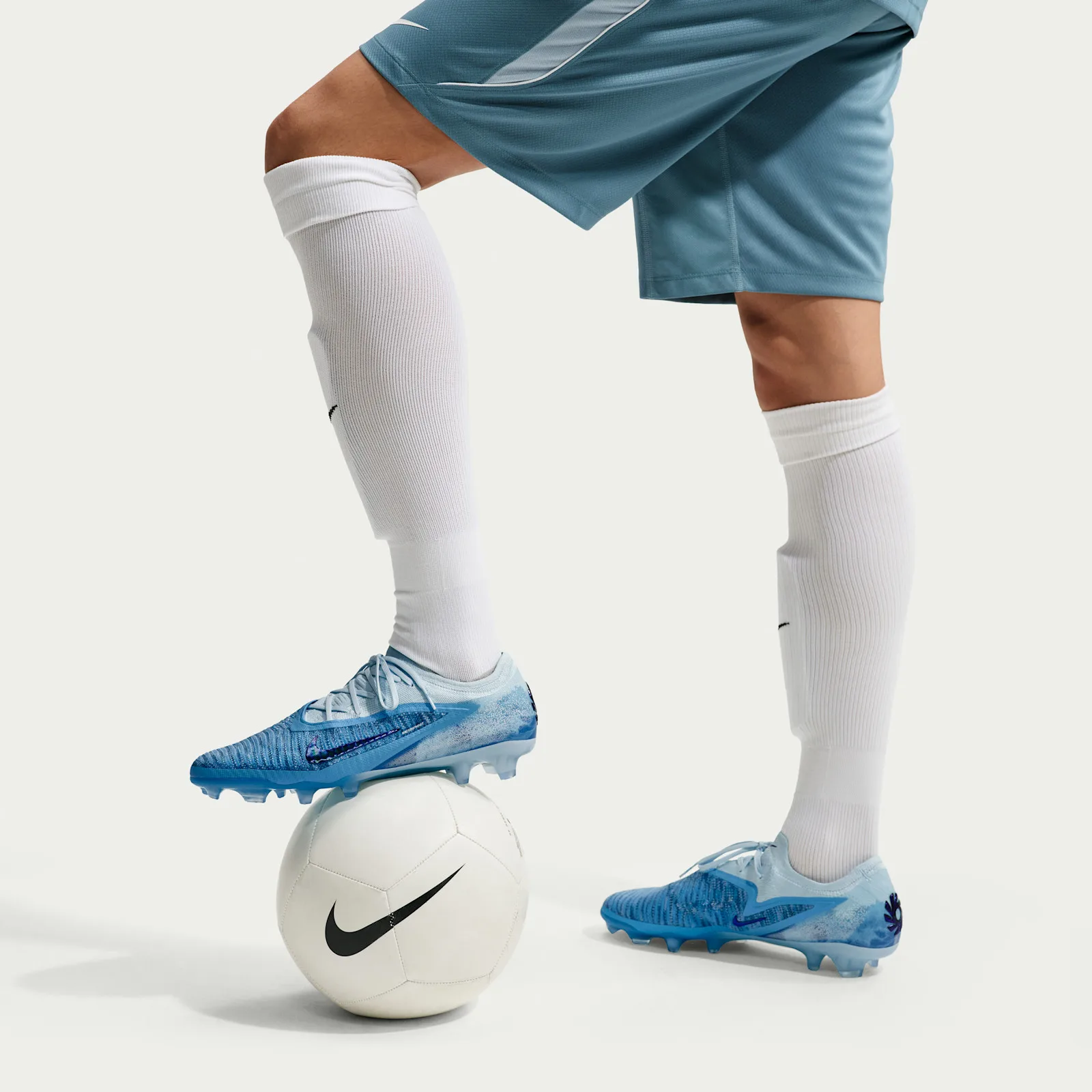 on-foot close-up, blue cleats resting on white soccer ball, white socks and shorts, Baltic Blue
