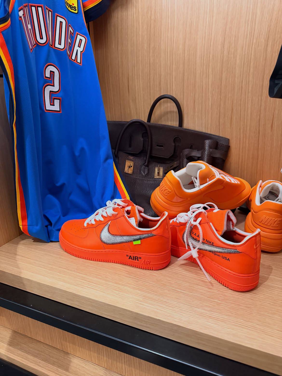 orange sneakers on shelf beside blue Thunder jersey and dark leather handbag, Nike Shai 001