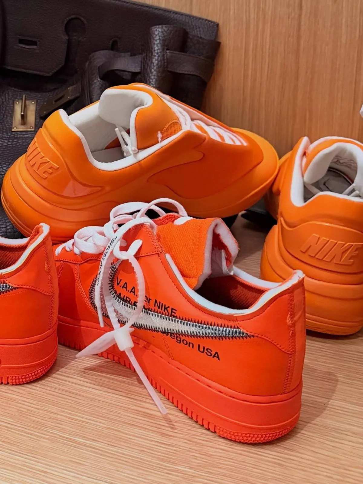 grouped orange sneakers on wood shelf with 'V.A.A. for NIKE' zigzag stitch text, Nike Shai 001