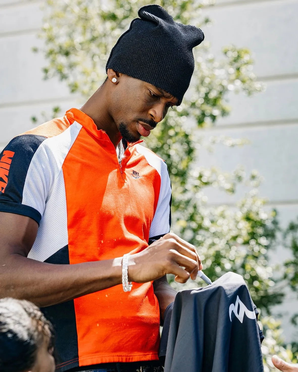 Close-up torso in an orange, white and black colourblock jersey with Nike swoosh, beanie, Nike SHAI 002