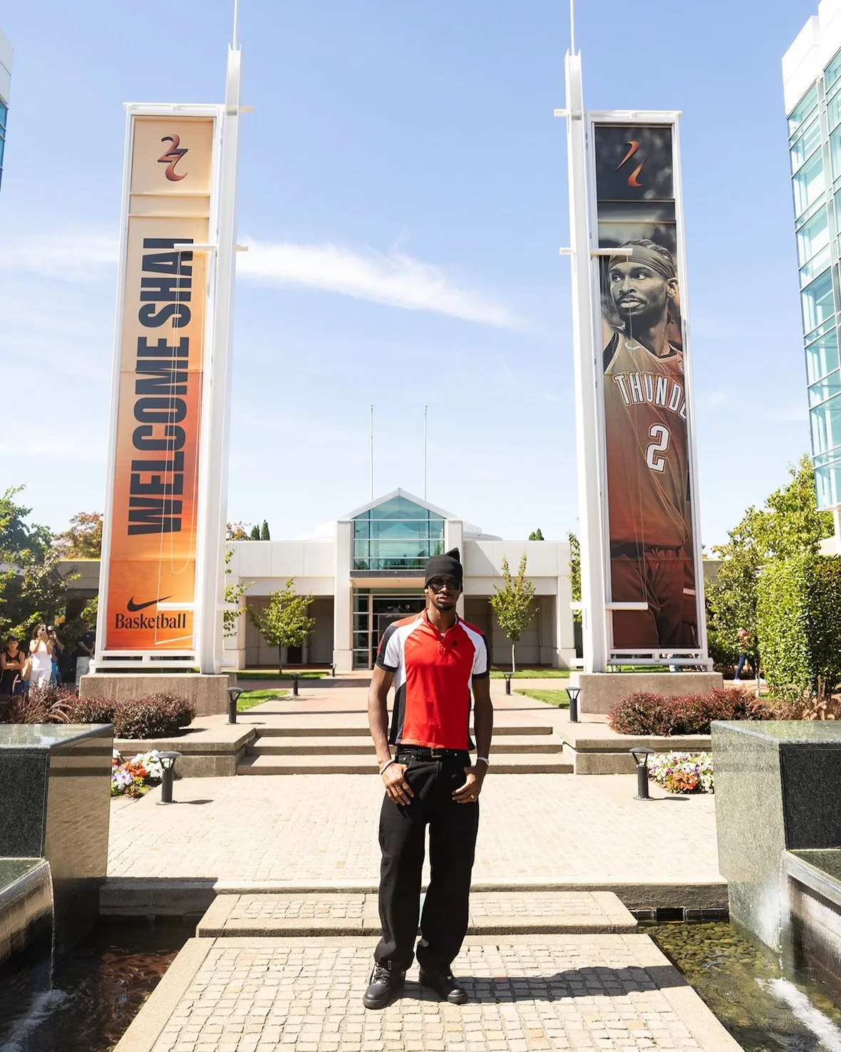 Full-body shot between tall 'Welcome Shai' banners, orange jersey, black sneakers, Nike SHAI 002