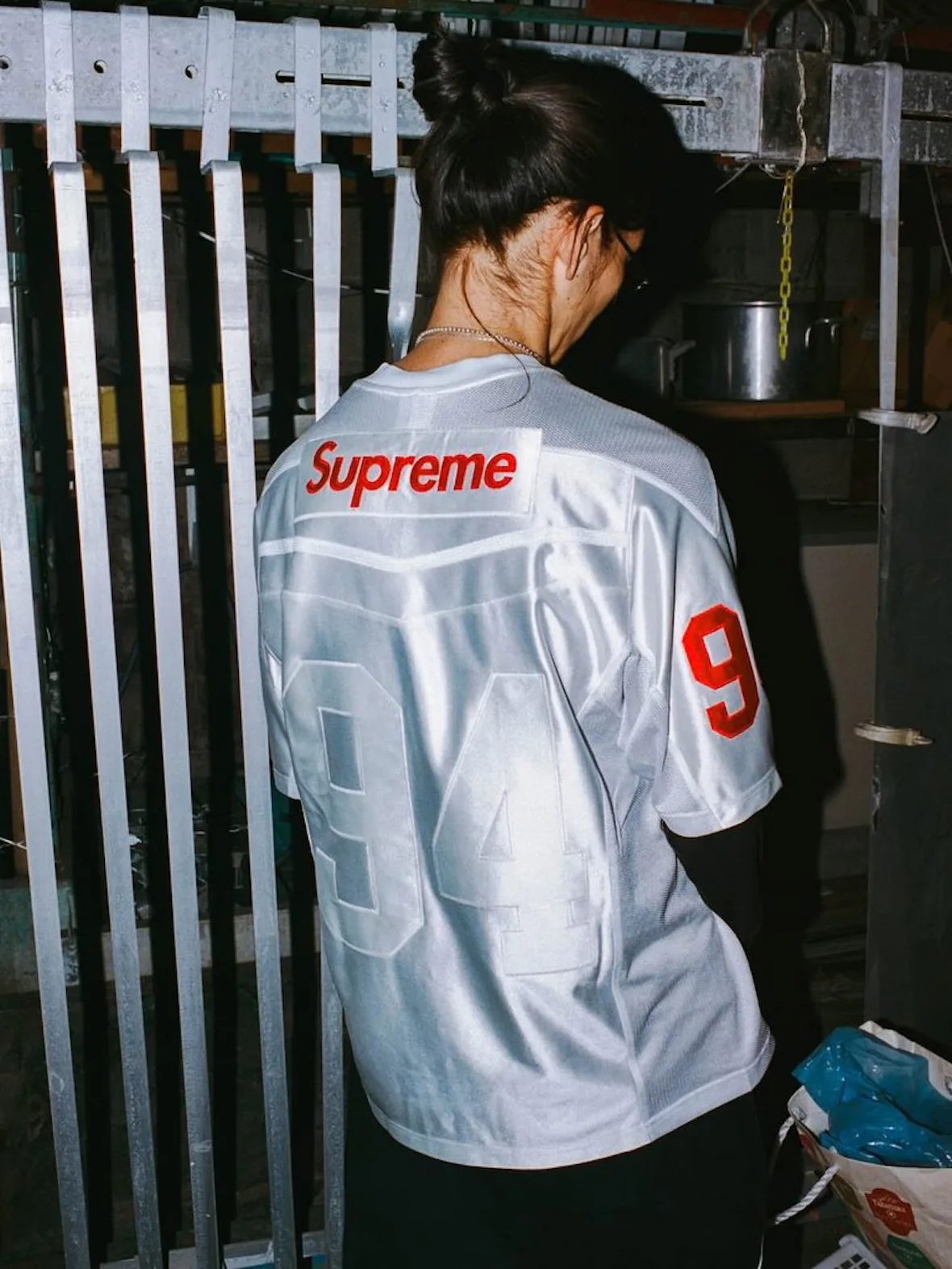 back view, silver-grey Supreme jersey with red logo and number 94, metal fence, Fall 2026 Collection