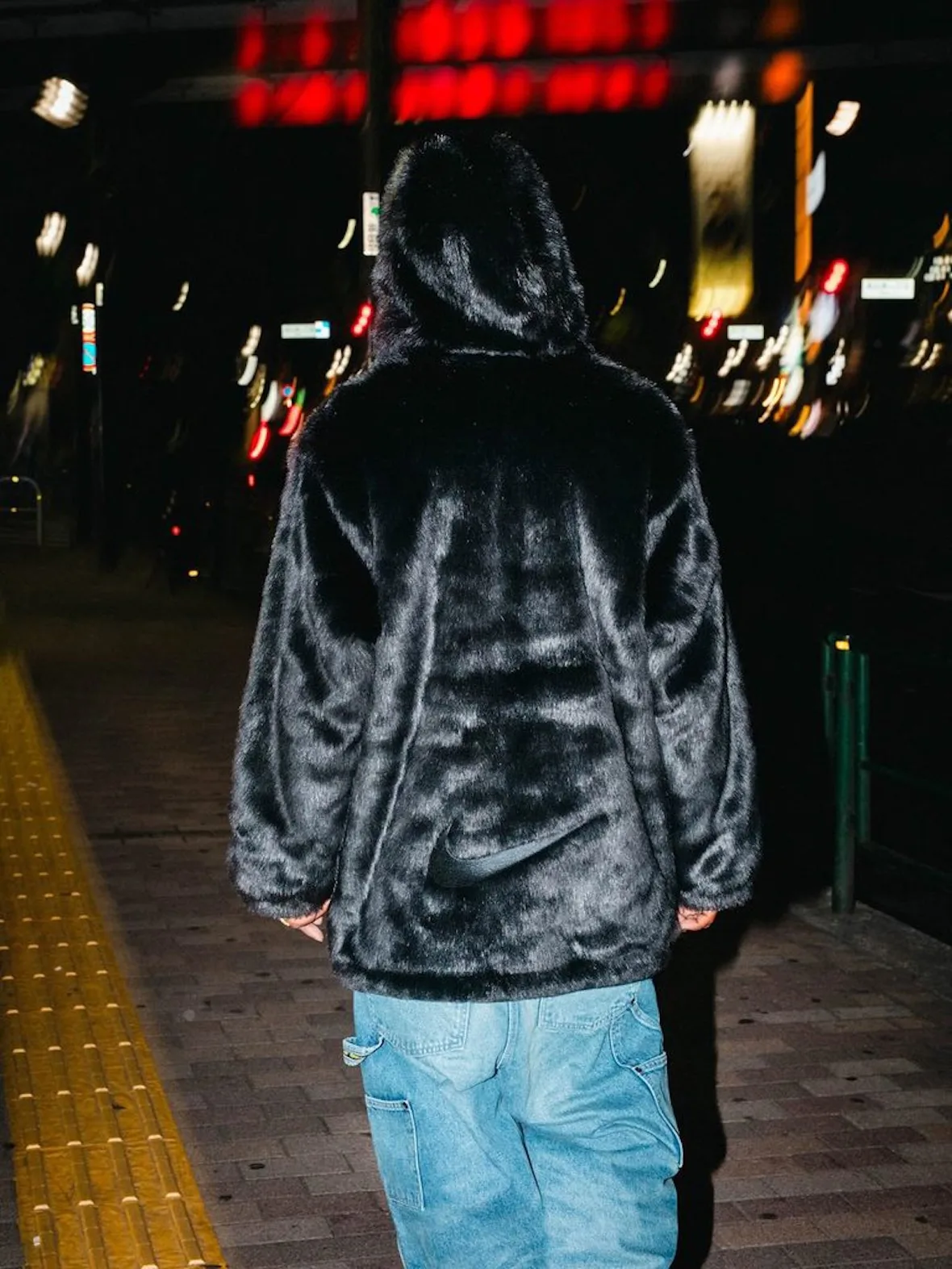 back view, black faux-fur jacket with Nike swoosh, light blue jeans, night street, Fall 2026 Collection