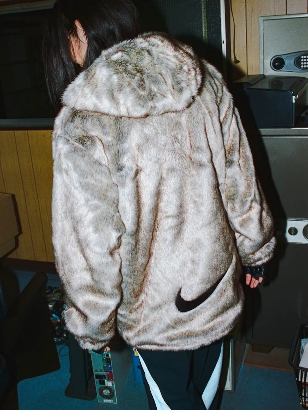 close-up back, cream faux-fur jacket with black Nike swoosh, cluttered indoor scene, Fall 2026 Collection