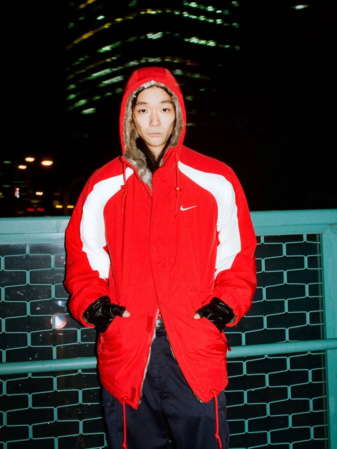 front view, red hooded jacket with fur-trimmed hood and Nike swoosh, night skyline, Fall 2026 Collection