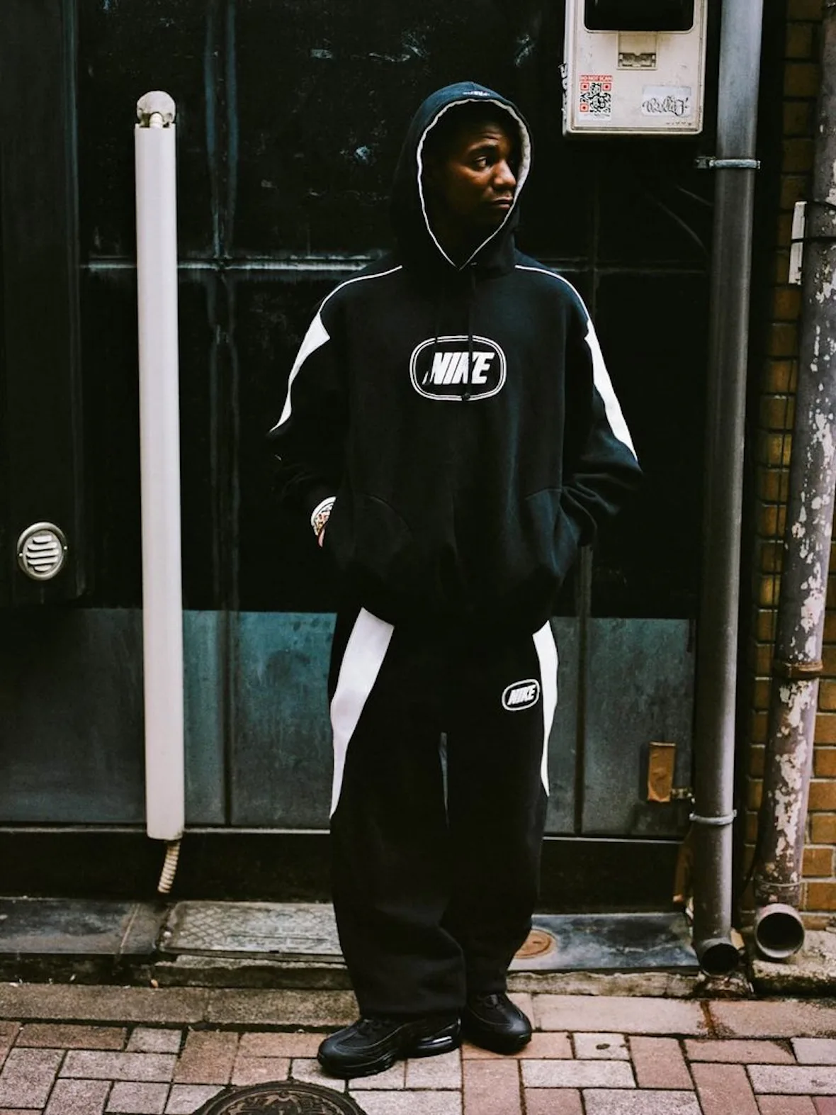 front view, black tracksuit with white stripe and oval Nike logo patch, alley, Fall 2026 Collection