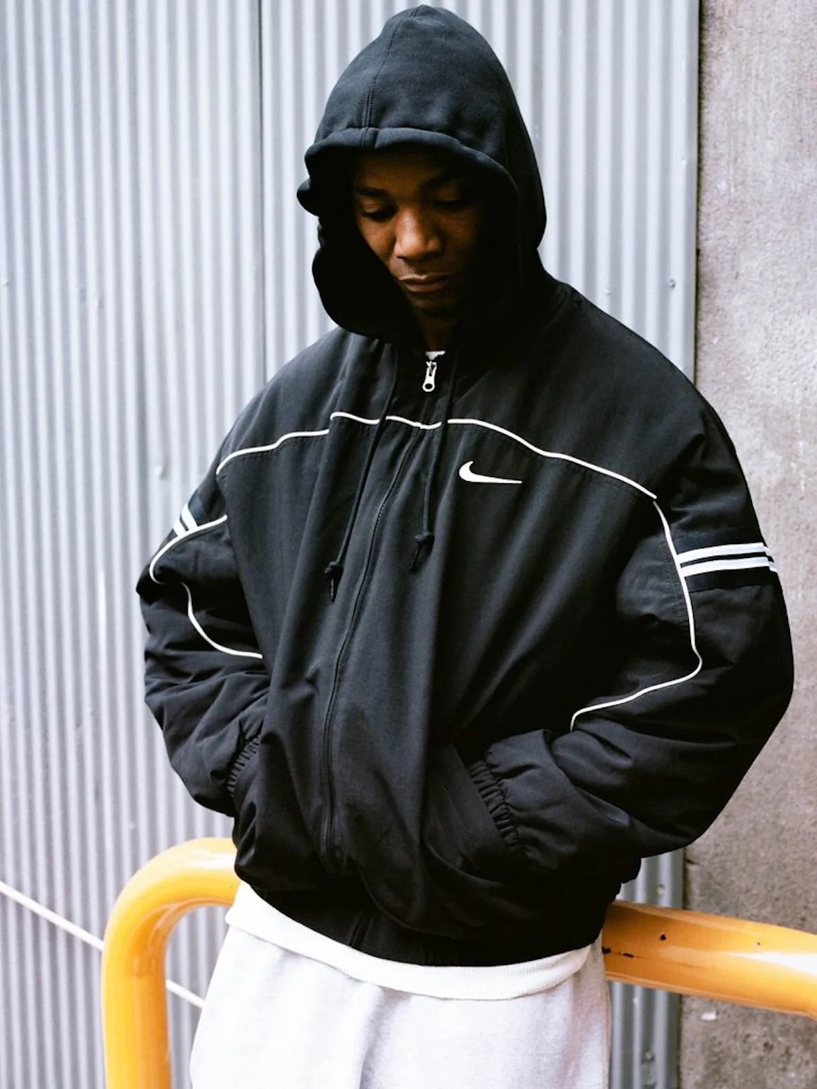 front view, black hooded jacket with white piping and Nike swoosh, corrugated wall, Fall 2026 Collection