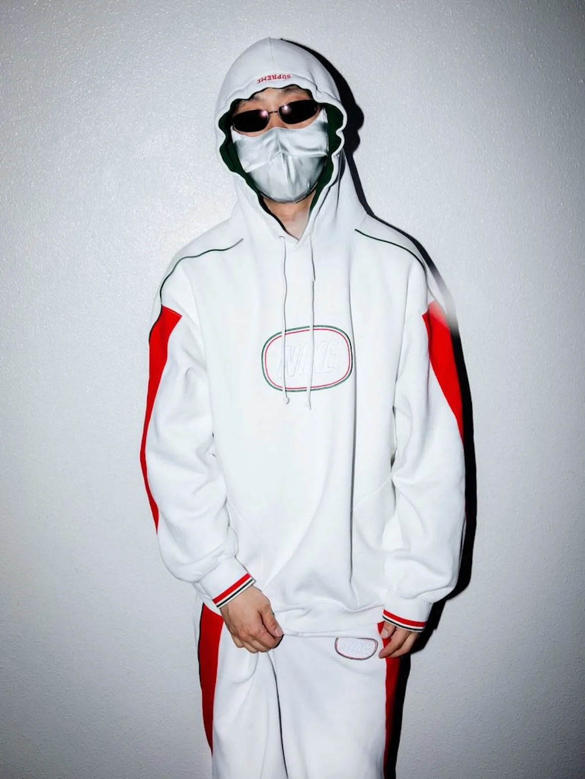 front view, white tracksuit with red stripe and oval Nike logo patch, grey face mask, Fall 2026 Collection