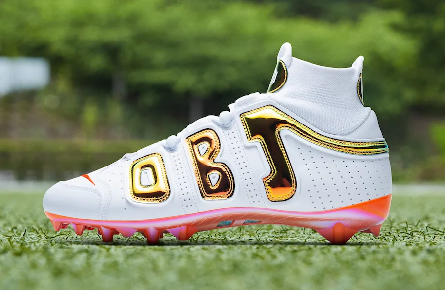 lateral view, white upper with gold 'OBJ' lettering, pink-orange outsole, OBJ Uptempo Cleat