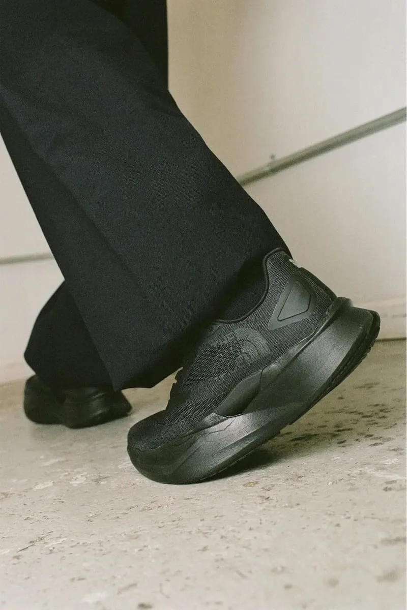 on-foot medial close-up, black knit upper and midsole against pale wall, Garments VECTIV Forward