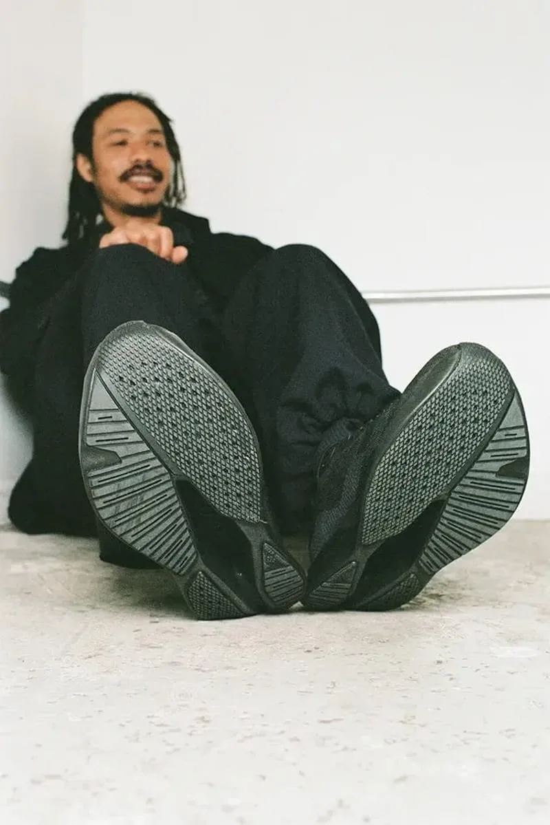 soles-forward view of seated man's black shoes, deep tread pattern visible, Garments VECTIV Forward