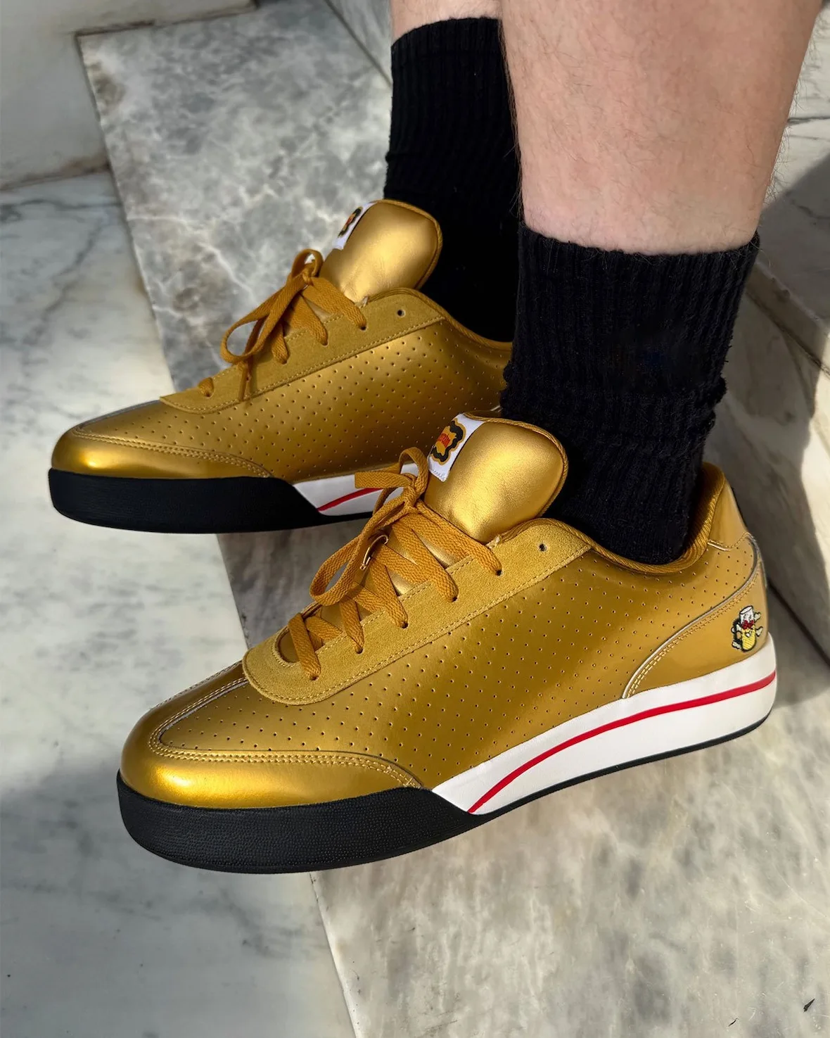 on-foot lateral, gold sneaker with black socks, red and white outsole stripe, Japanese Beer Pack