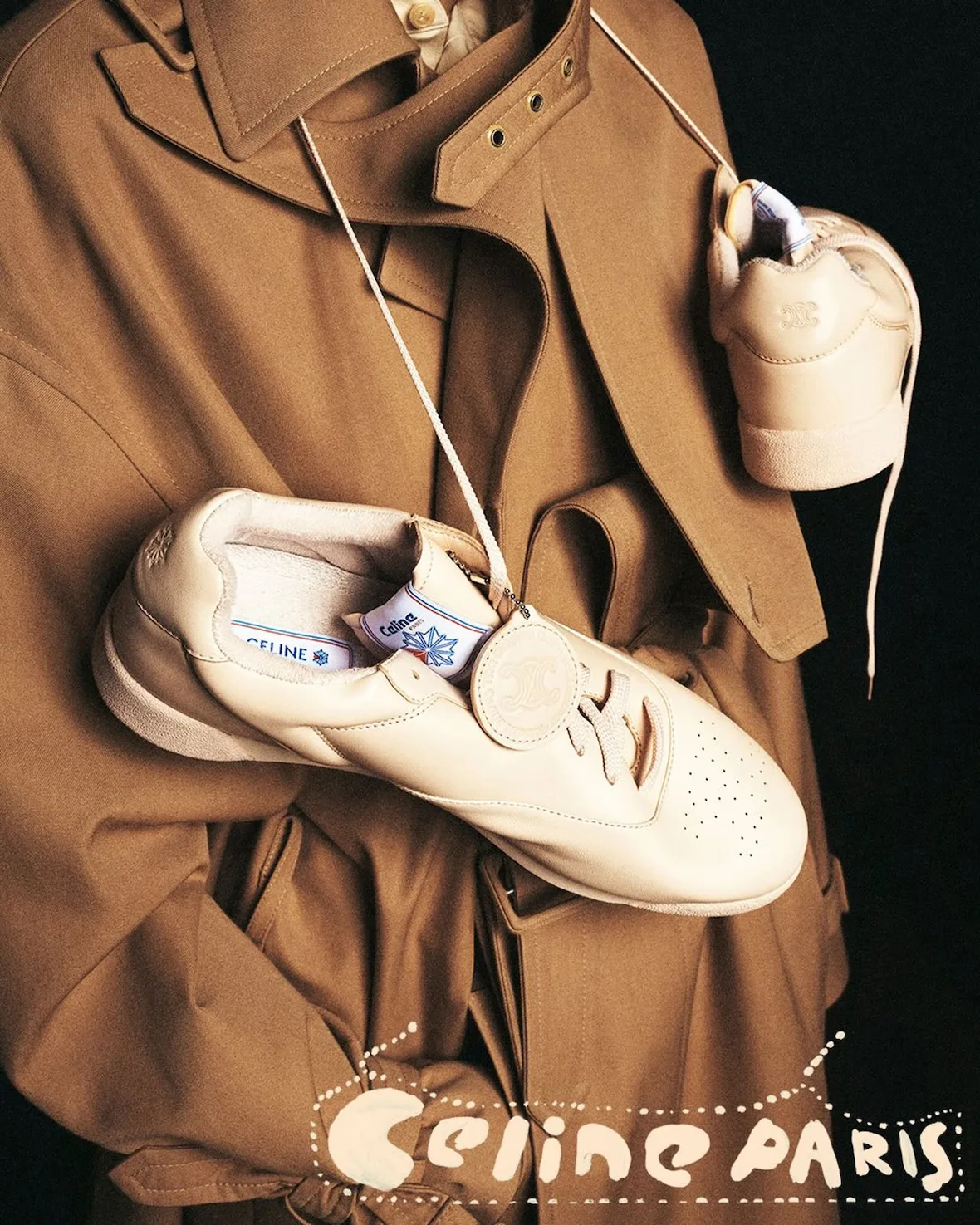 In-hand pair, cream leather sneakers dangling from a cord, Lo x Celine
