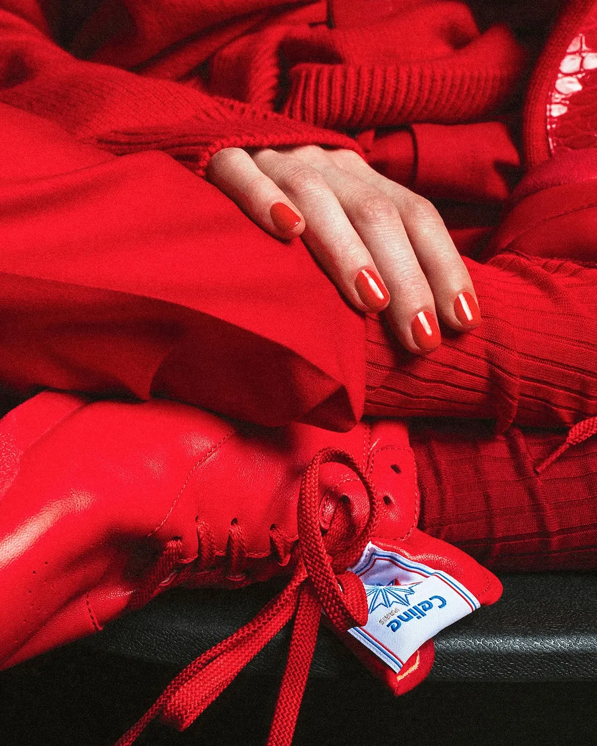 In-hand detail, red leather sneaker held by hand with red nail polish, Lo x Celine