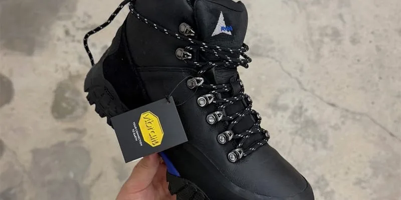 In-hand close-up of laced collar with ROA triangle logo and yellow hangtag, design Andreas Boot