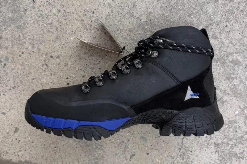 Lateral view on concrete, black boot with blue midsole and hangtag laces, design Andreas Boot