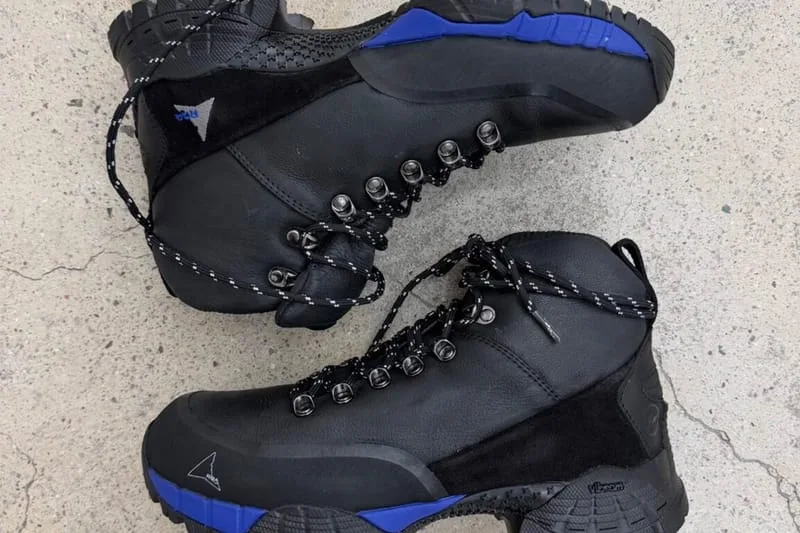 Pair of boots on concrete, one on its side showing blue-trimmed Vibram outsole, design Andreas Boot