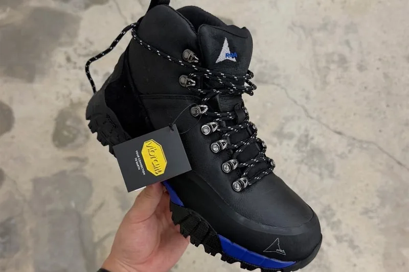 Toe-down in-hand view holding boot with yellow branded hangtag, blue midsole strip, design Andreas Boot