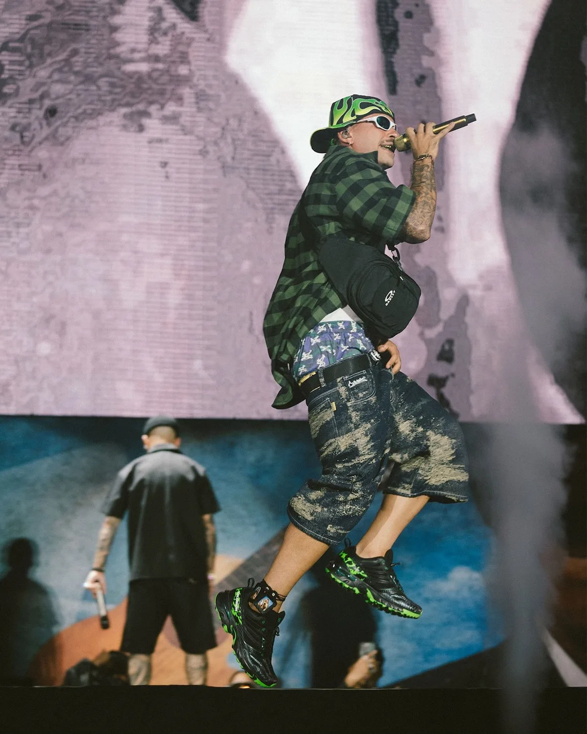 on-foot, black and green pair mid-jump on stage under green flame-print cap, NEXXT x Feid