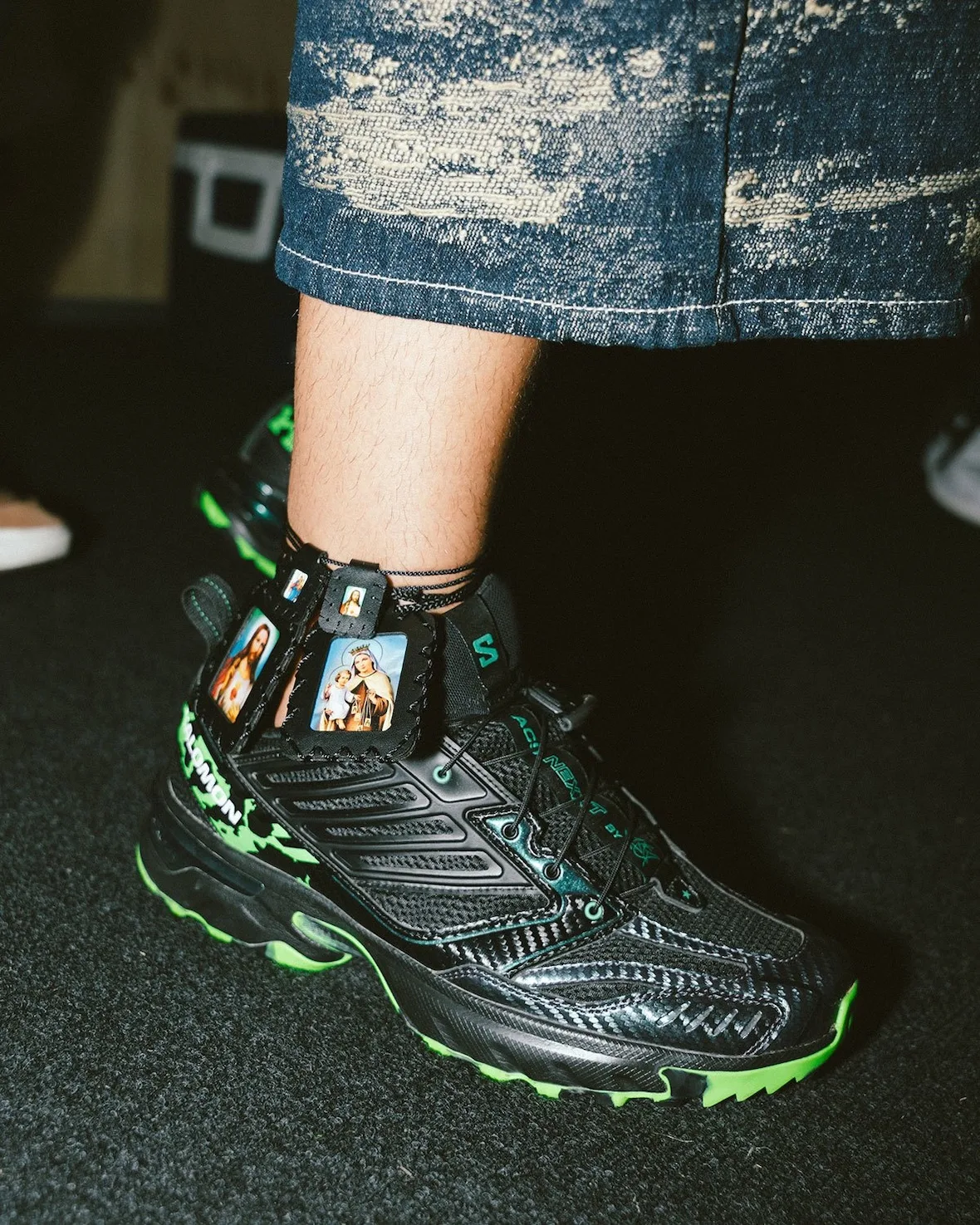 on-foot lateral close-up, black and green upper with religious icon ankle tags, NEXXT x Feid