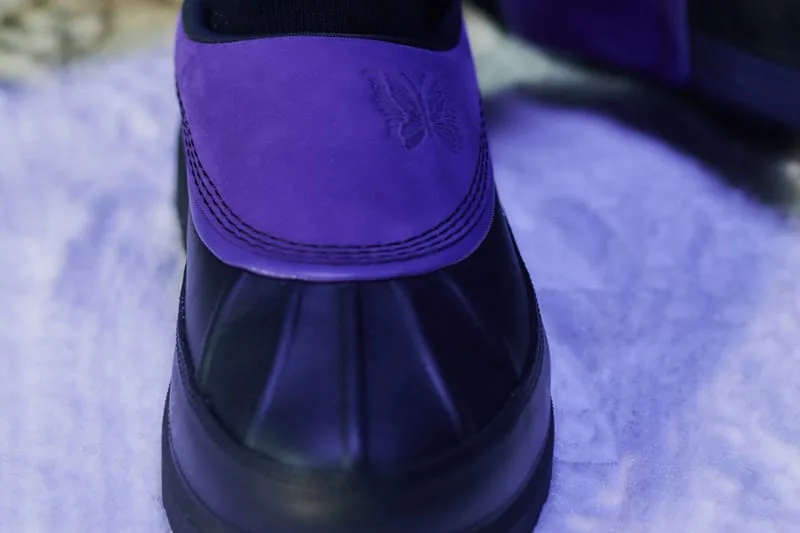 Heel close-up showing embossed butterfly logo on purple suede above black shell, NEEDLES Ambler Collection