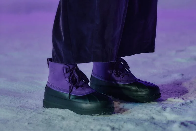 On-foot lateral view of purple duck boots with black soles on snow, velvet trousers, NEEDLES Ambler Collection