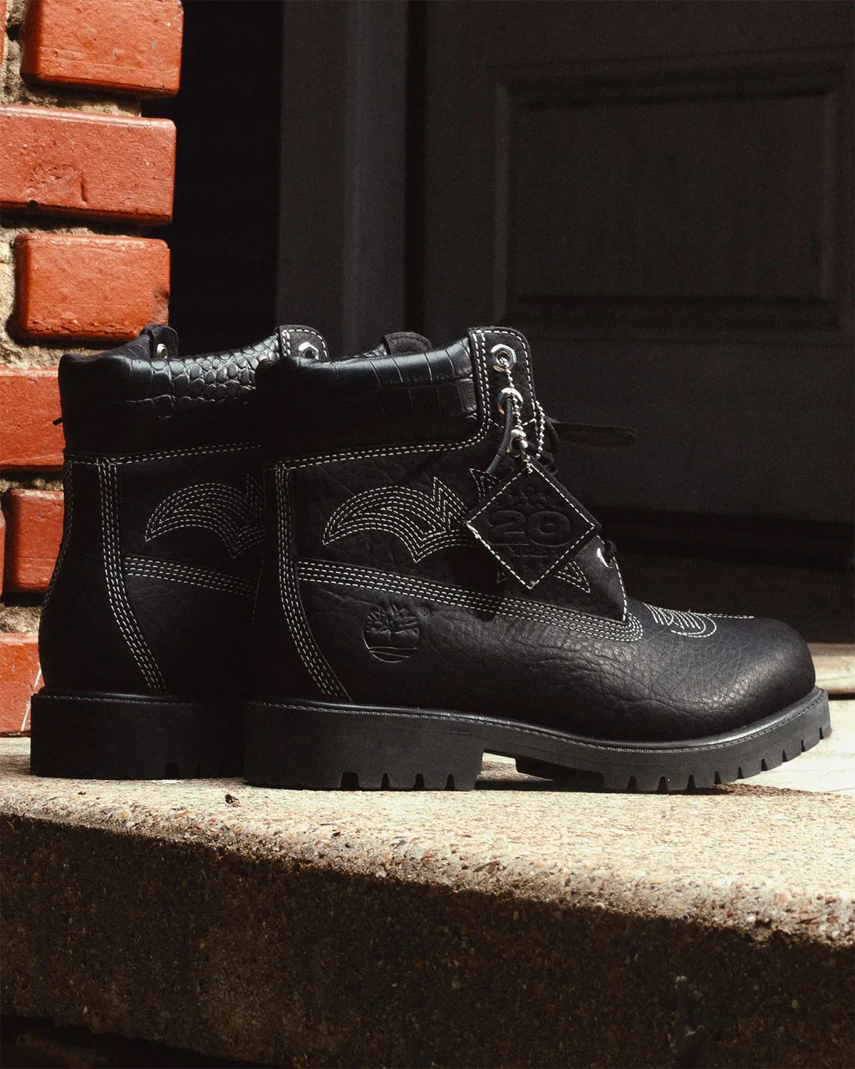 lateral view of black pair on stone step, 20-year tag hangs from laces, x Sneaker Politics