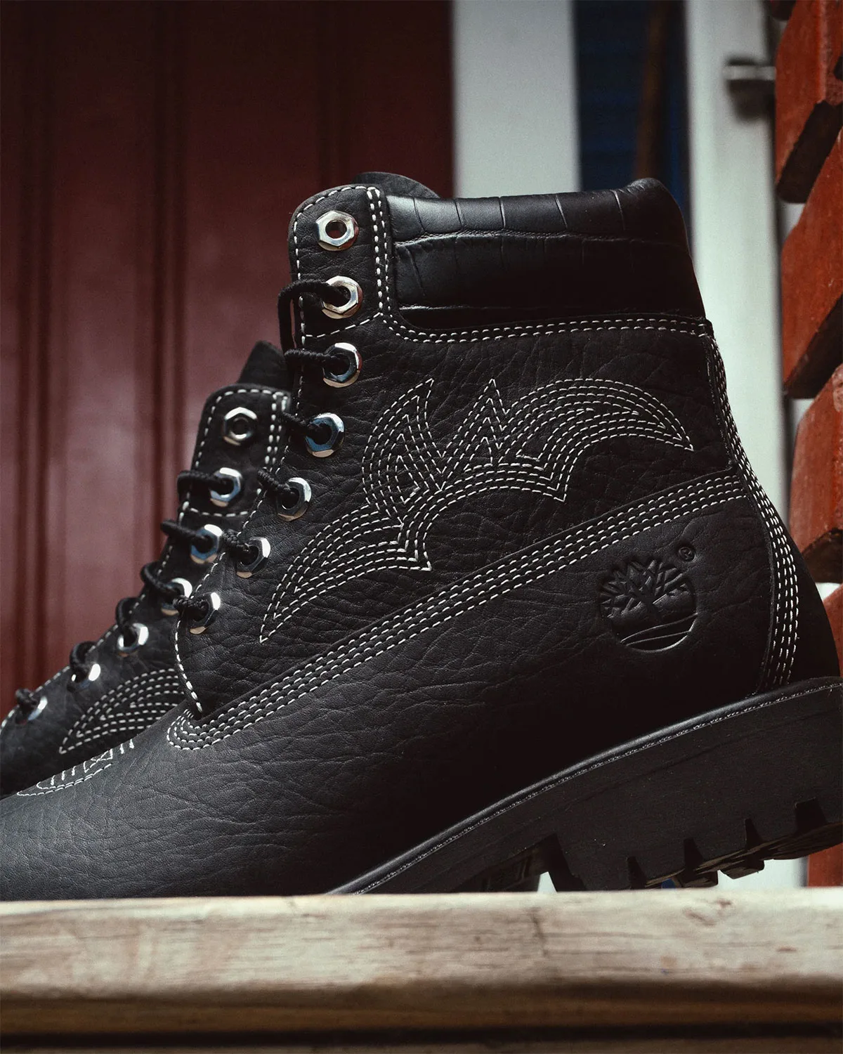 medial close-up of black pair, tan stitching, tree logo, brick backdrop, x Sneaker Politics