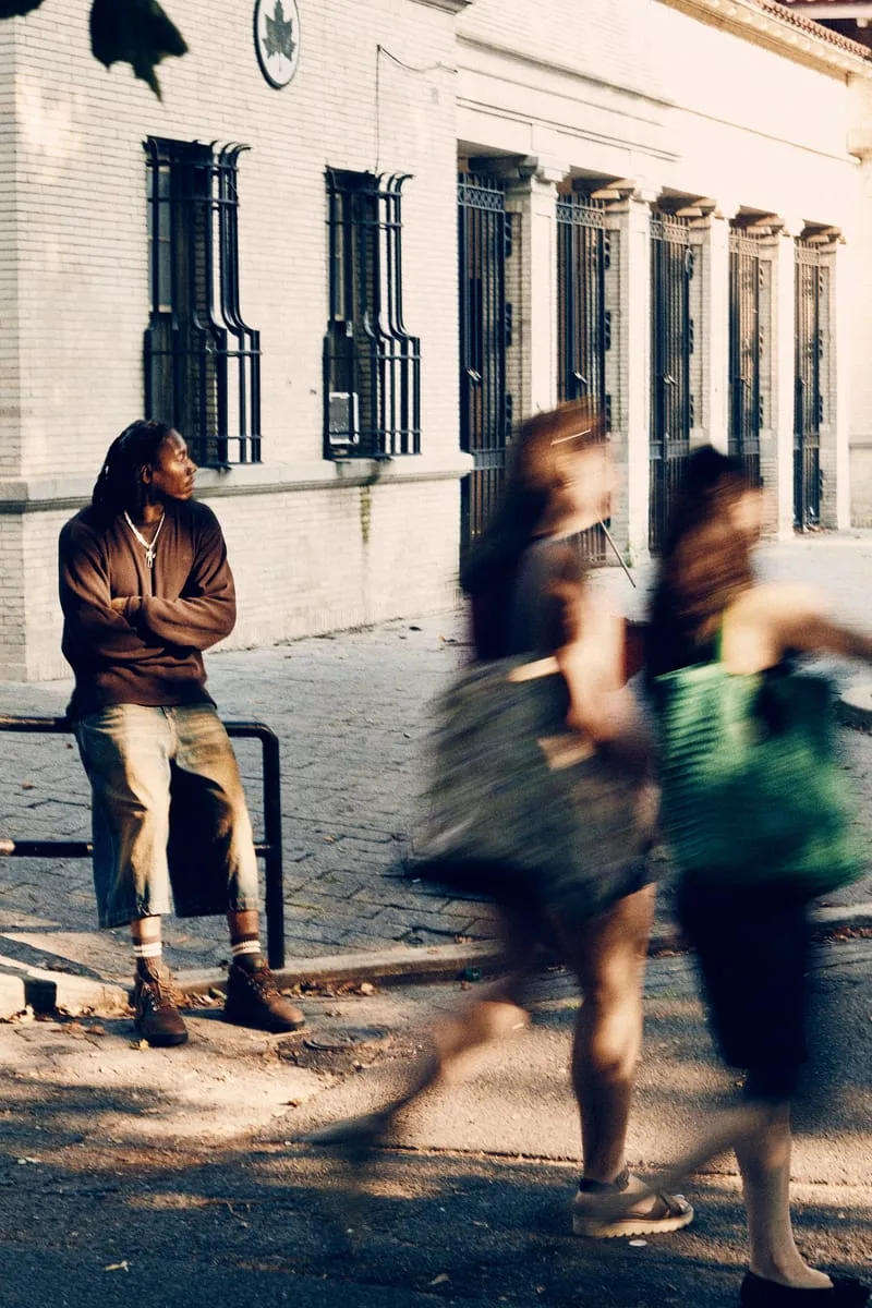 on-foot distant shot, man seated on railing near barred storefront, Timberland Field Boot