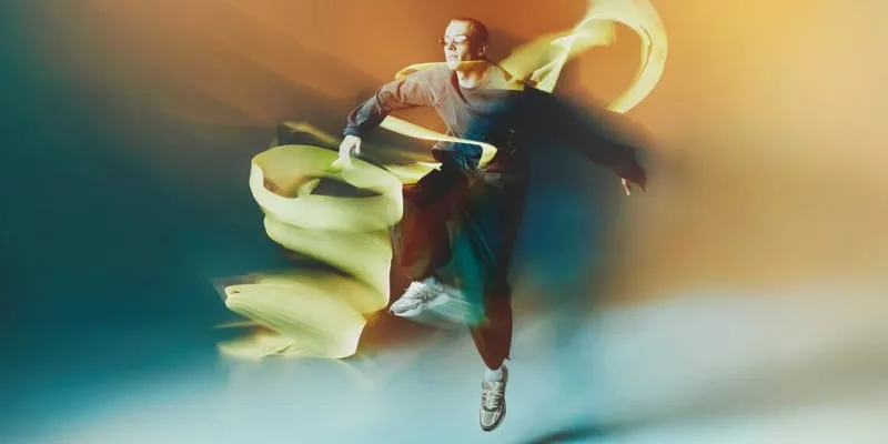 on-foot wide shot, grey pair worn mid-jump with yellow fabric swirls, orange backdrop, Tomorrowland WR1