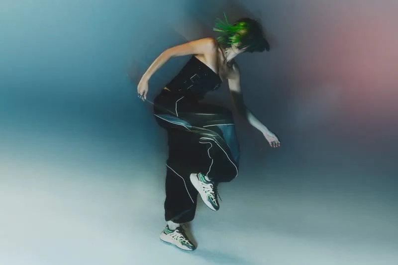 on-foot side view, white pair with green accents mid-motion, teal backdrop, Tomorrowland WR1