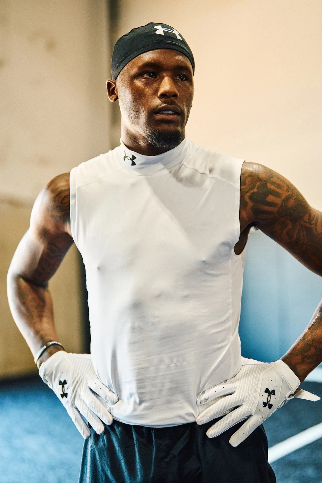 torso-up shot, hands on hips, white sleeveless top, black cap, white UA gloves, x Under Armour