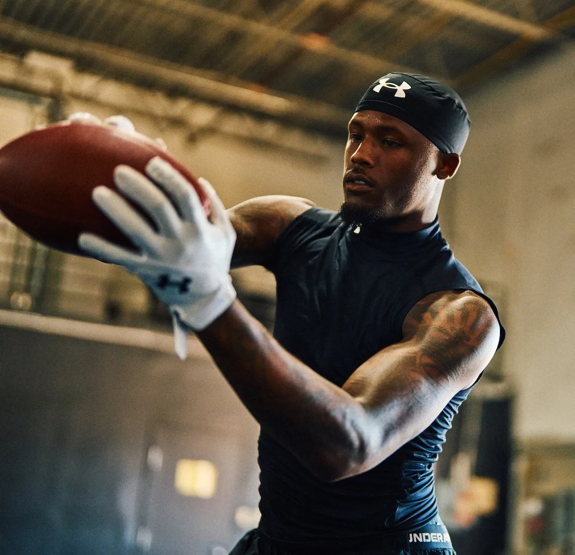 action shot catching a football, black skull cap, navy top, white UA gloves, x Under Armour