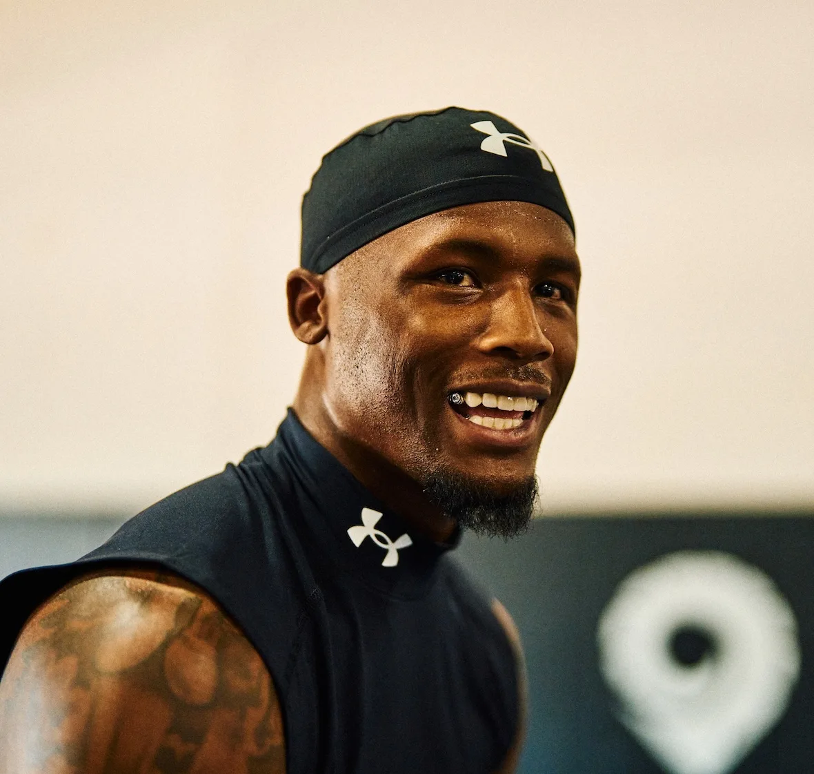 close-up portrait smiling, black skull cap and top, blurred pin-icon backdrop, x Under Armour
