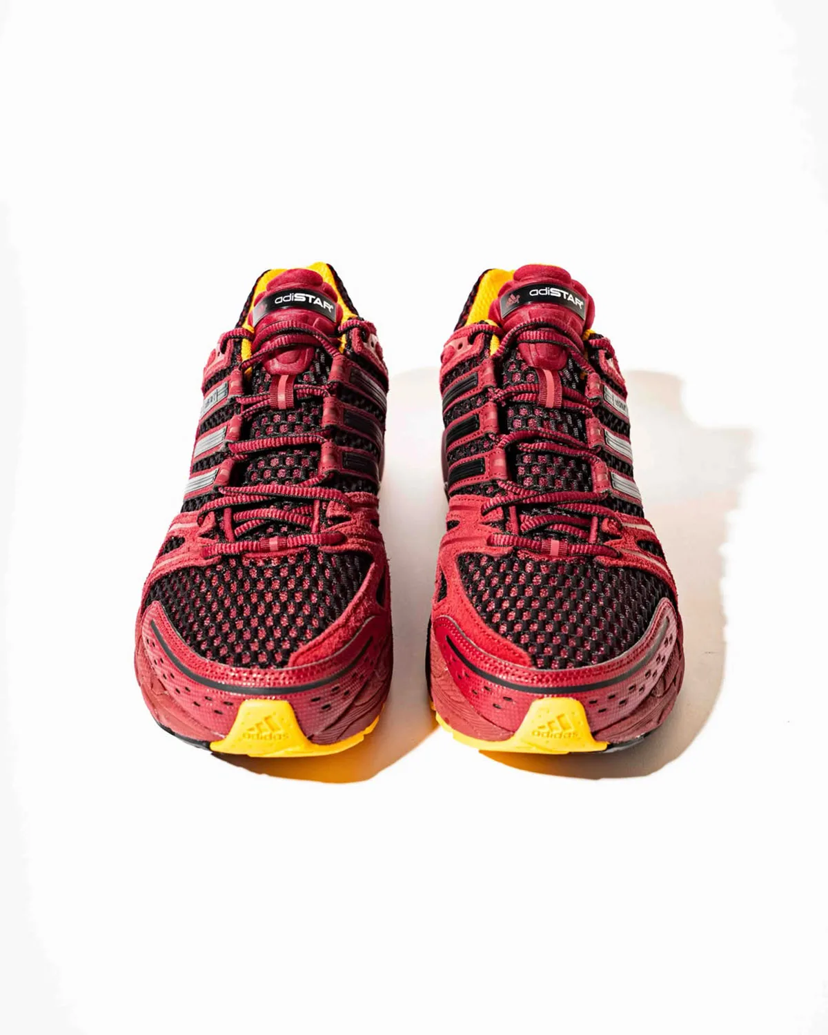 Toe-on view of a pair, burgundy and black mesh, yellow toe bumpers, adiSTAR tongue label, x Deadstock Coffee