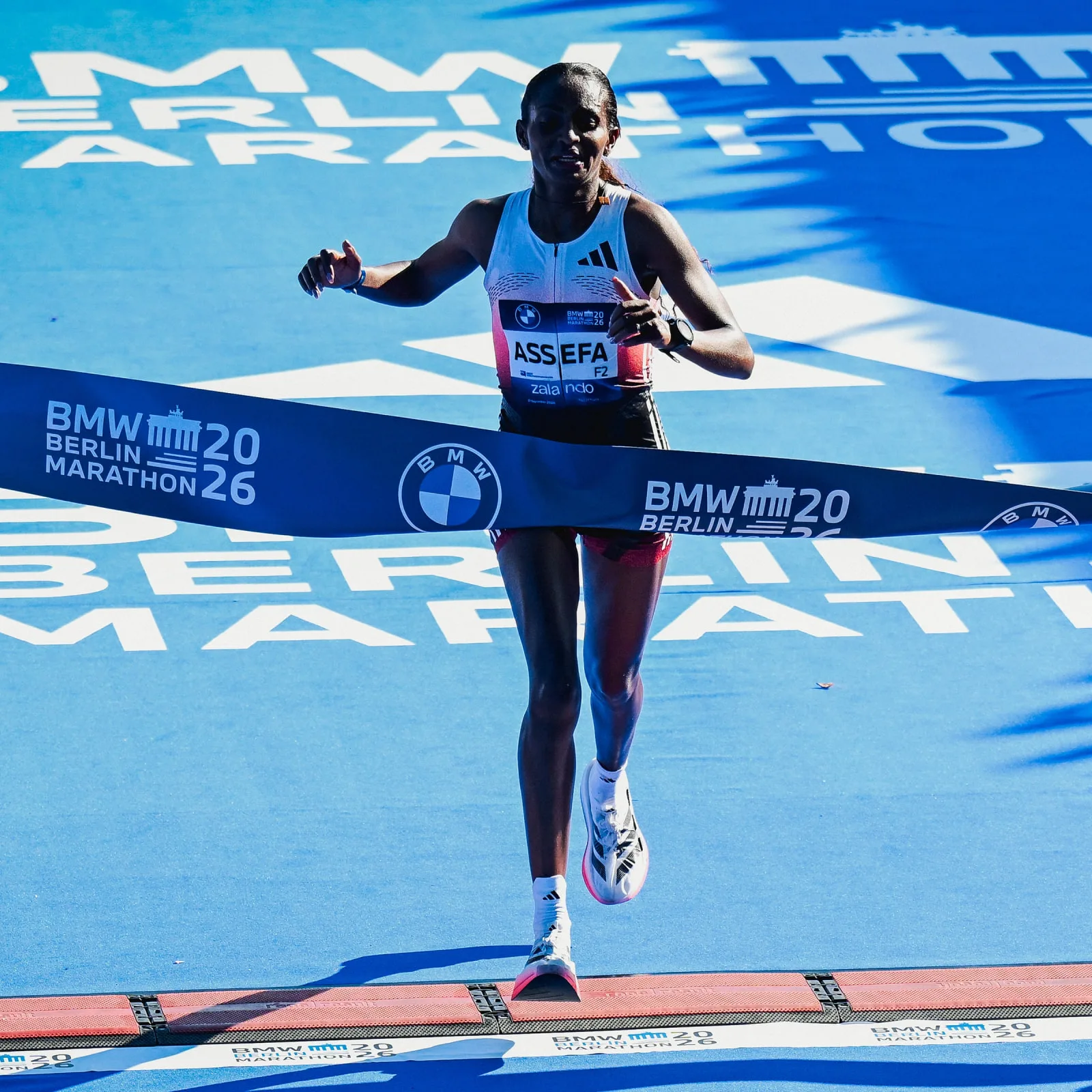 Runner in white vest crossing a BMW Berlin Marathon finish tape on blue ground, shoes mid-stride, Pro EVO 3