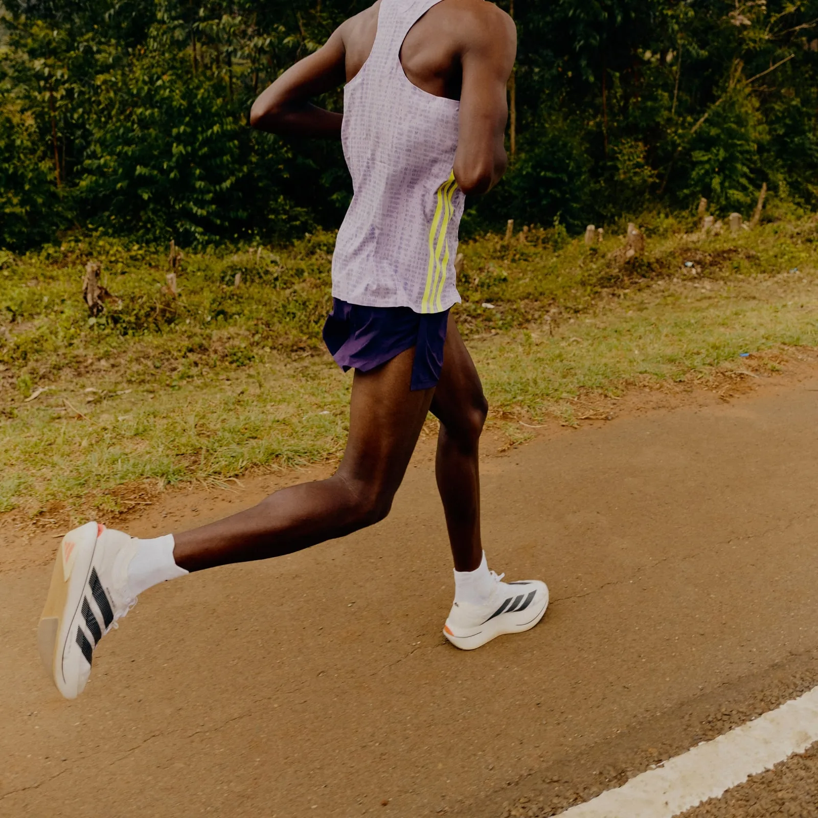 On-foot, runner mid-stride on a dirt road in purple vest and shorts, white shoes visible, Pro EVO 3