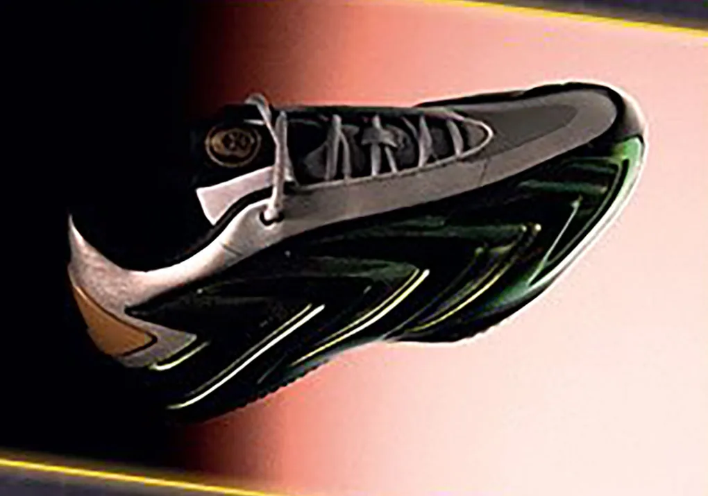 Tilted lateral view of a black sneaker with grey laces, gold tongue badge and neon-green outlined sole on a peach gradient