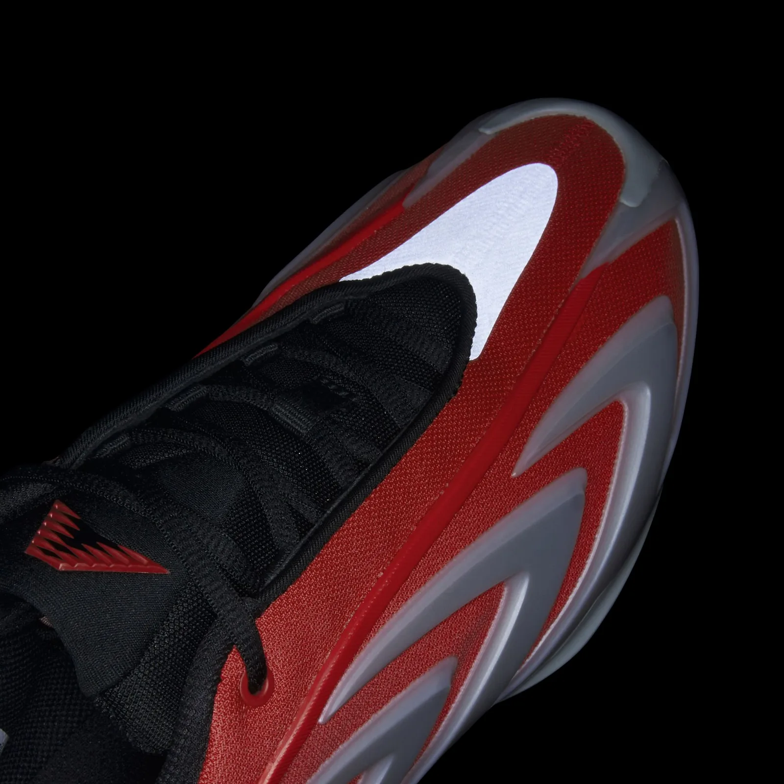 Detail on black background, reflective silver toe panel glowing white, red mesh and black laces, Omen