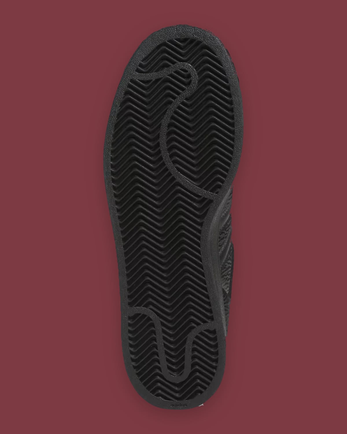 Outsole view: black zigzag herringbone tread with adidas text at the heel, on maroon background, Halloween