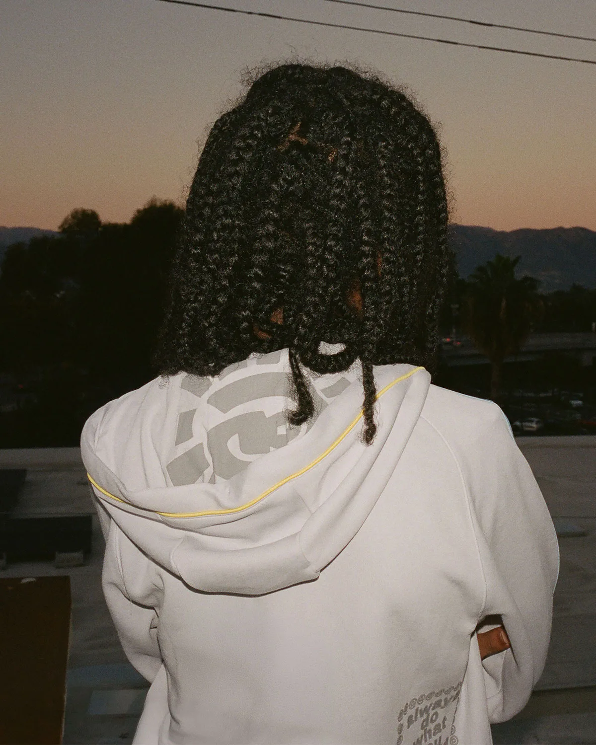 On-person rear view of braided hair and white hoodie with grey logo print at dusk, Climacool x ADWYSD