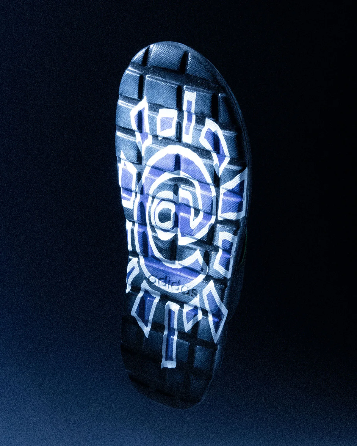 Outsole of flip-flop with large white sun logo over purple tread blocks on dark backdrop, Climacool x ADWYSD