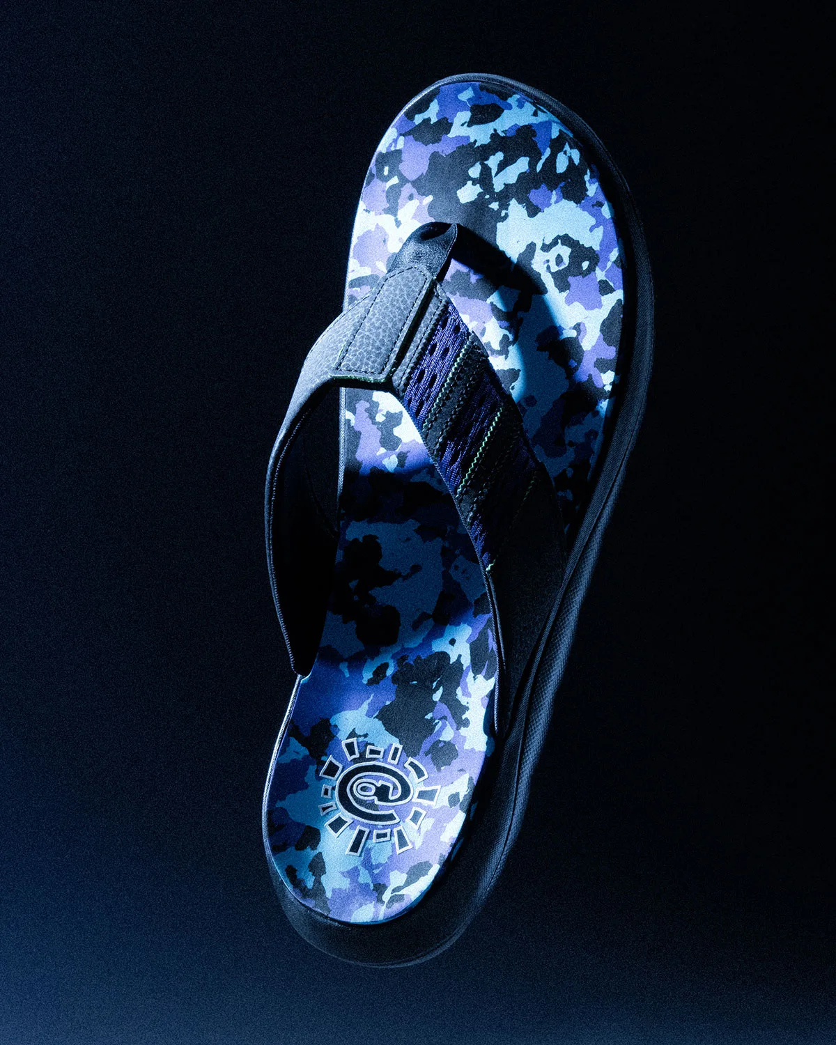 Top-down flip-flop with blue and purple camo footbed and sun logo, on dark backdrop, Climacool x ADWYSD